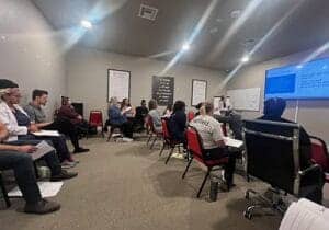 large group of men and women listen to behavioral therapist speak as part of a benzodiazepine addiction rehab program