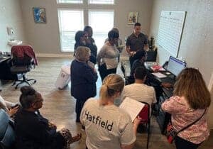 several men and women are gathered in a circle listening to a speaker as part of a heroin addiction rehab program